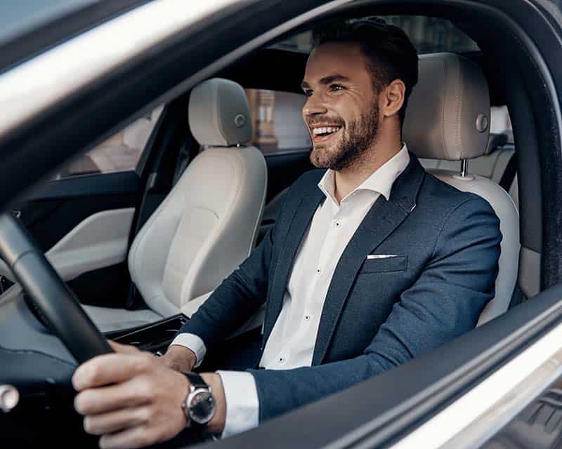 Smiling man in a business suit driving a car