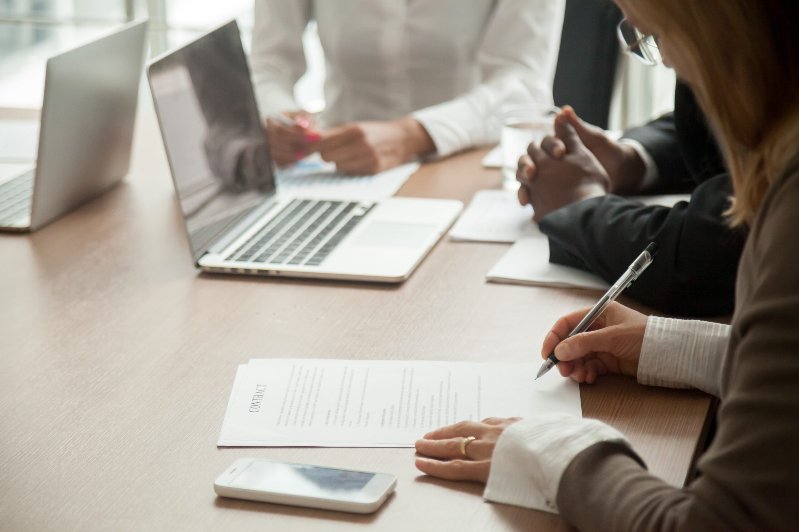 woman employee writing on a paper with co employees working on their laptop