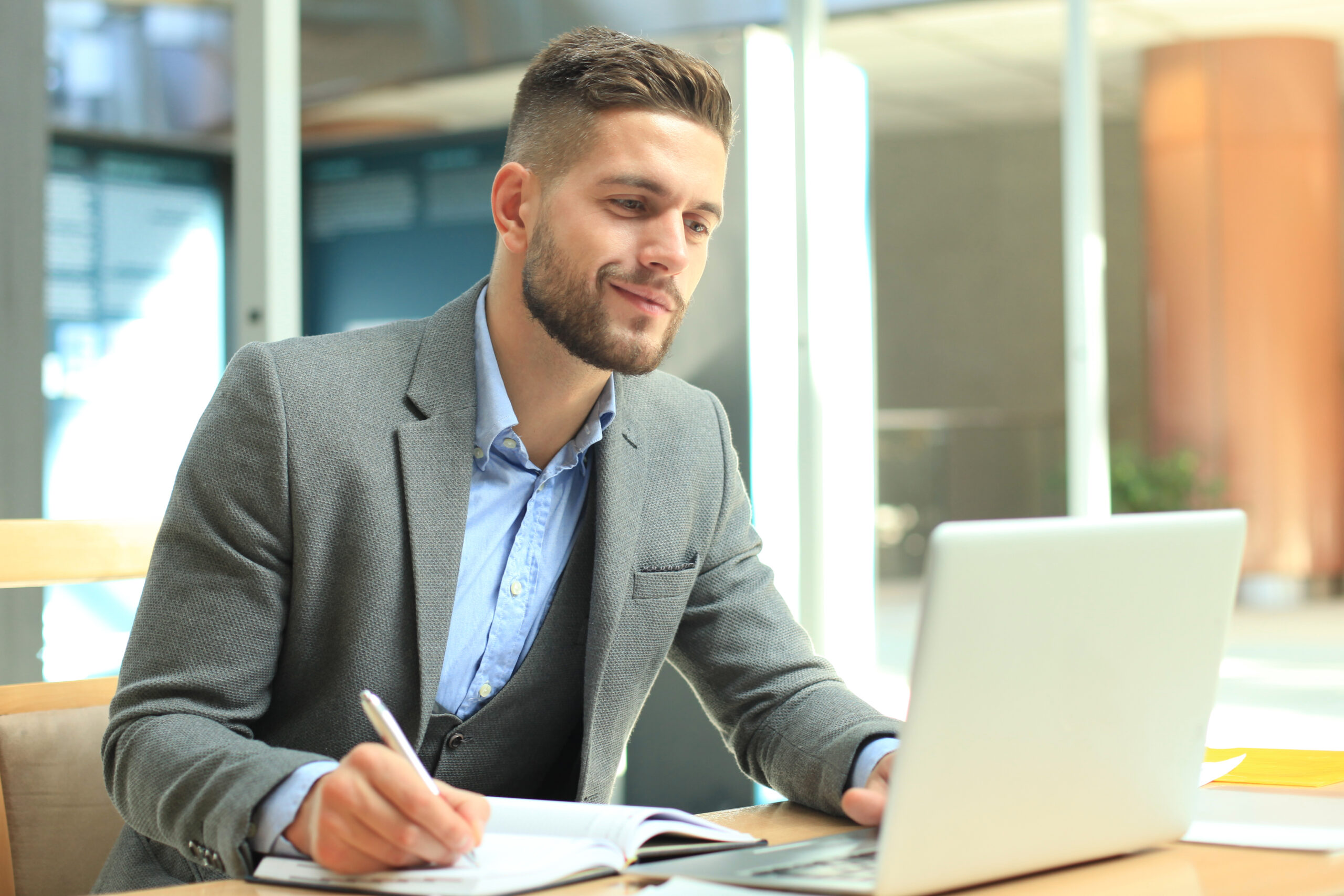 man in suit writing in front of the laptop